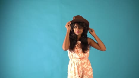 A-young-Indian-girl-in-orange-frock-wearing-a-hat-and-standing-in-an-isolated-blue-background