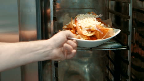 Placing-a-bowl-of-delicious-nacho's-with-cheese-in-a-industrial-oven