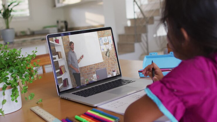 Ragazza afroamericana che fa i compiti mentre è in videochiamata con un insegnante uomo al laptop a casa.