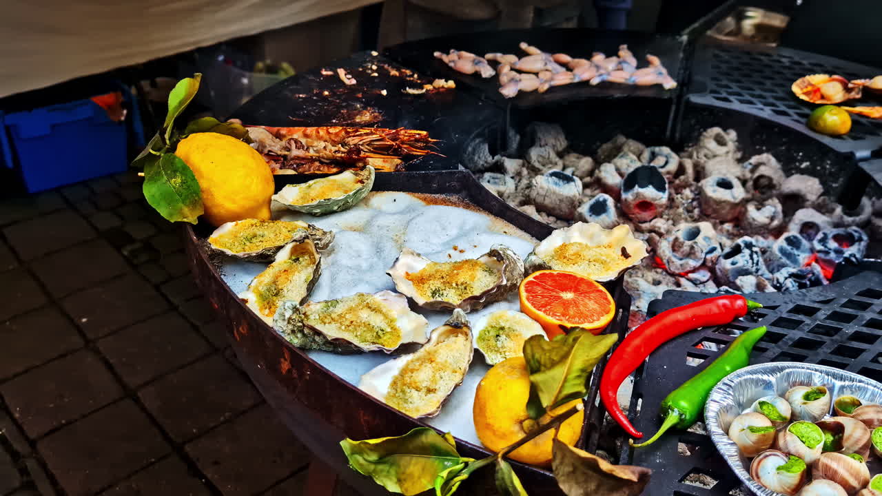 Oysters, escargot, and sausages cooking over a large open charcoal grill with citrus and peppers