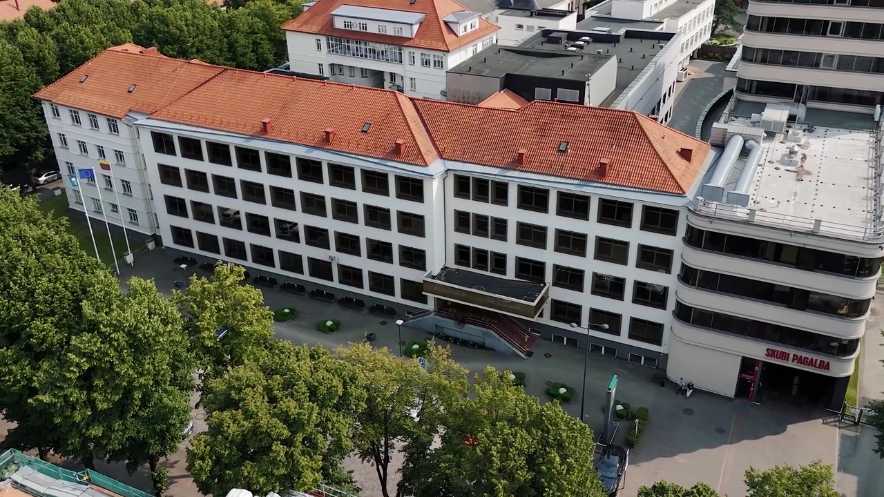 Edificio del Dipartimento di Emergenza dell'Ospedale Repubblicano di Klaipėda con tetto in tegole rosse e ingresso alberato in una lenta ripresa aerea.