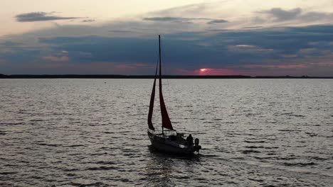 low aerial view of sailboat in silhouette on river during sunset with birds flying through frame