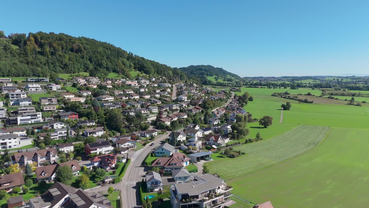 Main Street leading through luxury city of Zuzwil in Switzerland. Sunny day with blue sky and green fields. Noble houses and apartments in village. Wide shot. Drone flyover