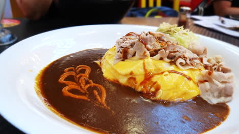 curry japonés con tocino de cerdo y tortilla de huevo encima de arroz japonés en un restaurante acogedor