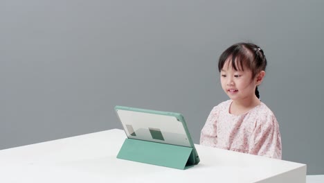 Child-using-digital-tablet-sitting-near-the-table-to-watch-cartoon