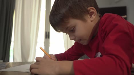 Caucasian-boy-painting-a-magic-lamp-draw-using-a-yellow-marker-indoors,-side-view,-bright-window-in-the-background-4K-pan