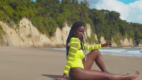 sexy modelo de bikini se sienta en la arena mientras las olas del océano chocan en el fondo y un épico cloudcape en la distancia