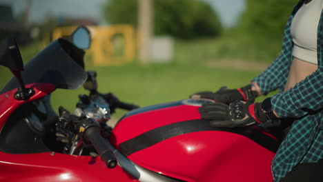 close-up of a female biker gently moving her hand from the motorcycle's tank to her waist, and then to her lap, she is wearing a red-and-black helmet, with a blurred background