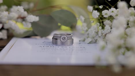 Anillos-De-Boda-Rodeados-De-Bebés-Que-Respiran-Flores-En-Una-Invitación-De-Boda.