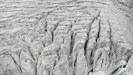 Aerial-view-of-the-Moiry-glacier-near-Grimentz-in-Valais,-Switzerland-with-a-panning-up-view-of-the-icy-crevasses-towards-the-clouds-hiding-the-mountain-peaks