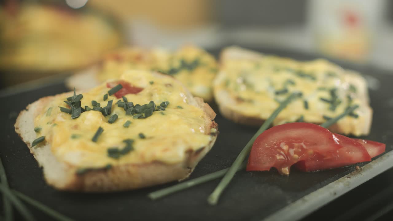primer plano de una tostada francesa vegana presentada con una rodaja de tomate y cebollino mientras un chef rocía la tostada con rodajas de cebollino