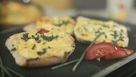 Close-up-of-vegan-french-toast-presented-with-a-tomato-slice-and-chive-while-a-chef-sprinkles-the-toast-with-chive-slices