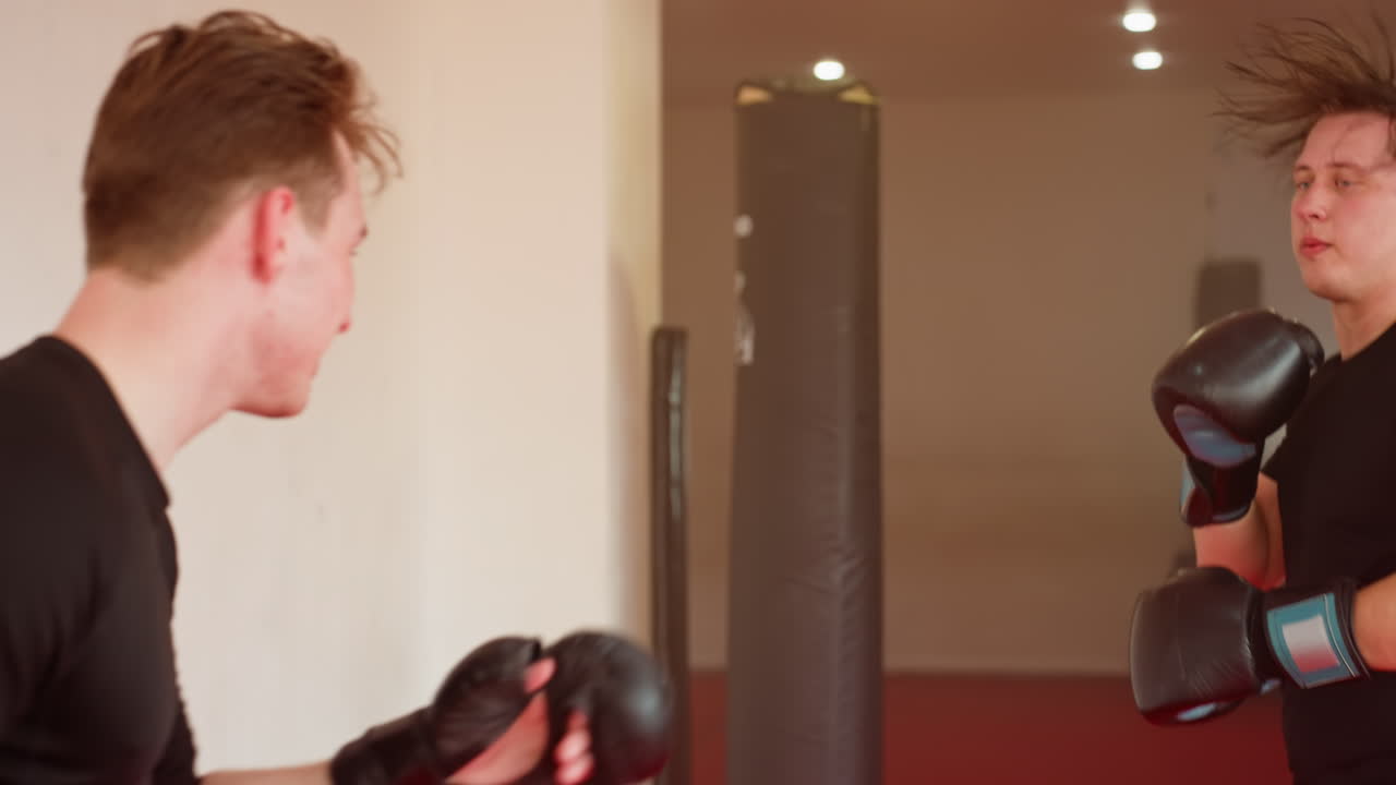 MMA fighter wearing black gloves and sportswear performing defensive stance during training inside gym, focused on movement and blocking while sweating from intense workout on red mat background
