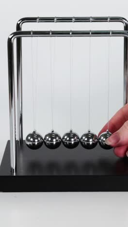 la mano pone en movimiento la cuna de newton.