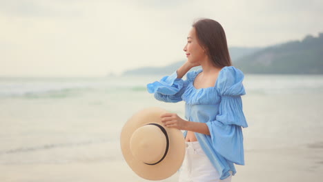 young asian woman walks on beach and puts her hat on