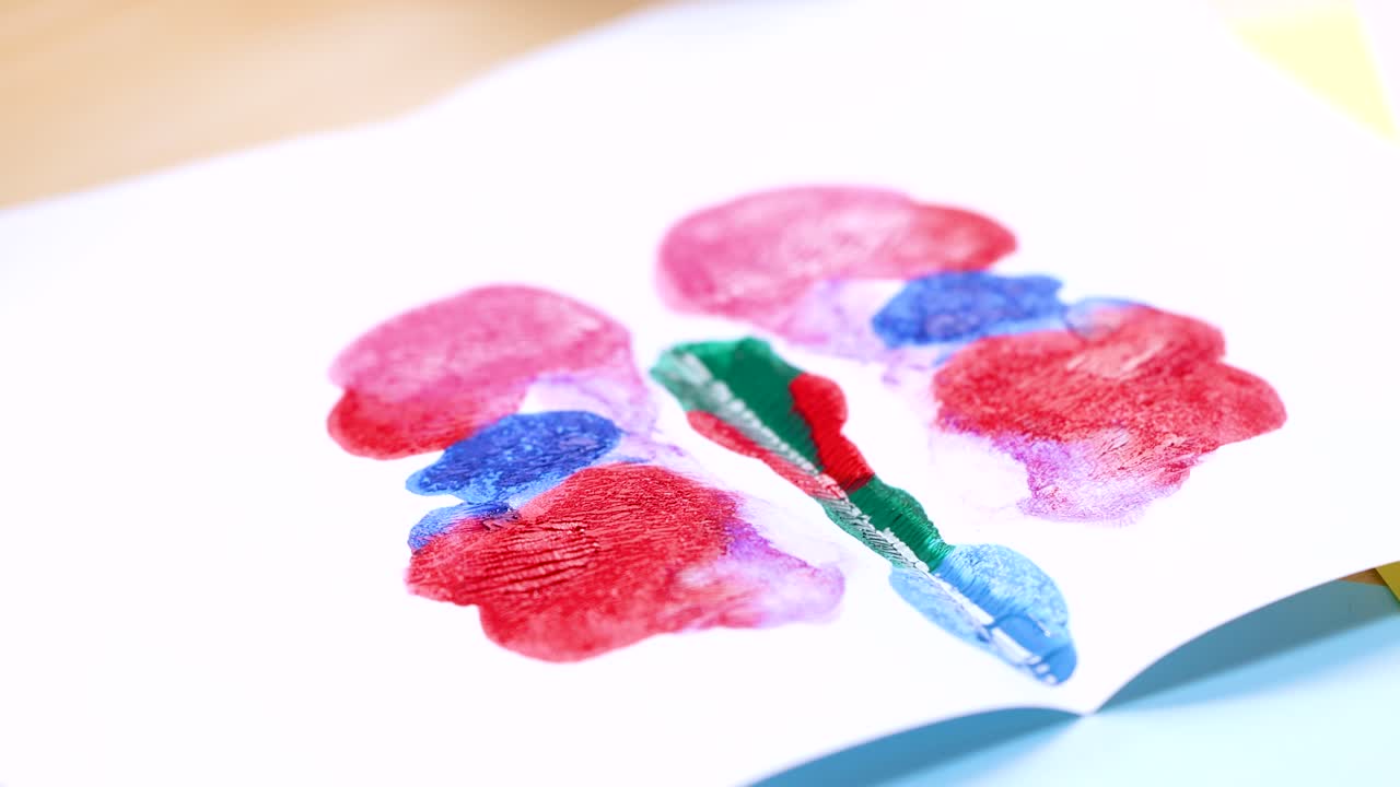 Child opens folded paper, revealing vibrant symmetrical butterfly created with acrylic paint, bright lighting