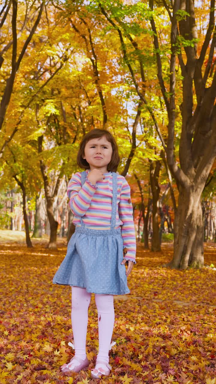 Happy young girl tosses a handful of vibrant orange and yellow maple leaves high up, standing on a ground covered with foliage in a beautiful sunny fall park