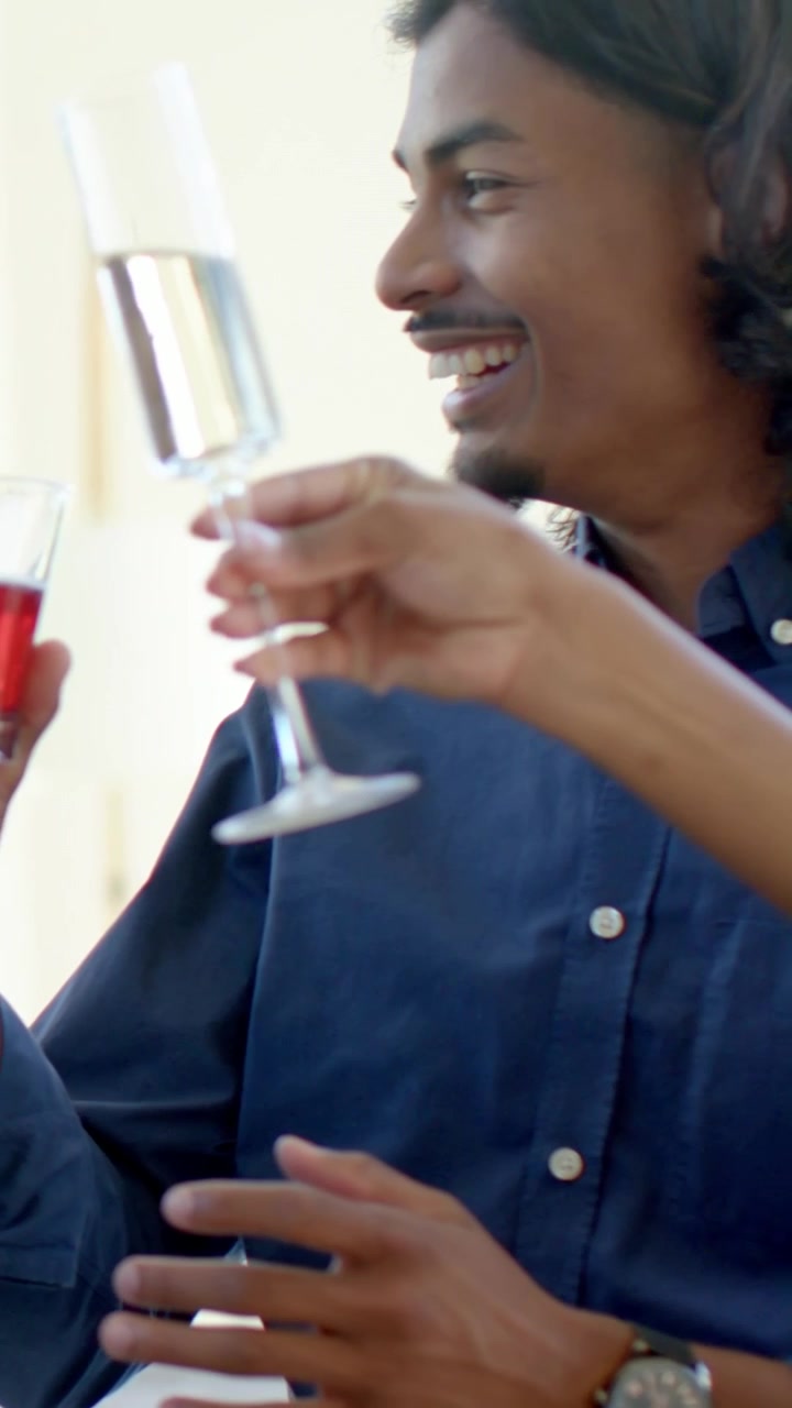 Vertical video: Meeting glasses sparking man in blue shirt raising toast in sunroom, with tumblers
