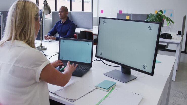 Caucasian businesswoman sitting using laptop in office with male coworker in background