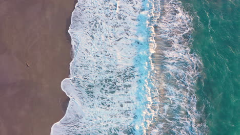 Drohne-Senkt-Sich-Langsam-über-Türkisfarbenes-Meer-Und-Strand-Und-Wellen,-Die-An-Land-Kommen