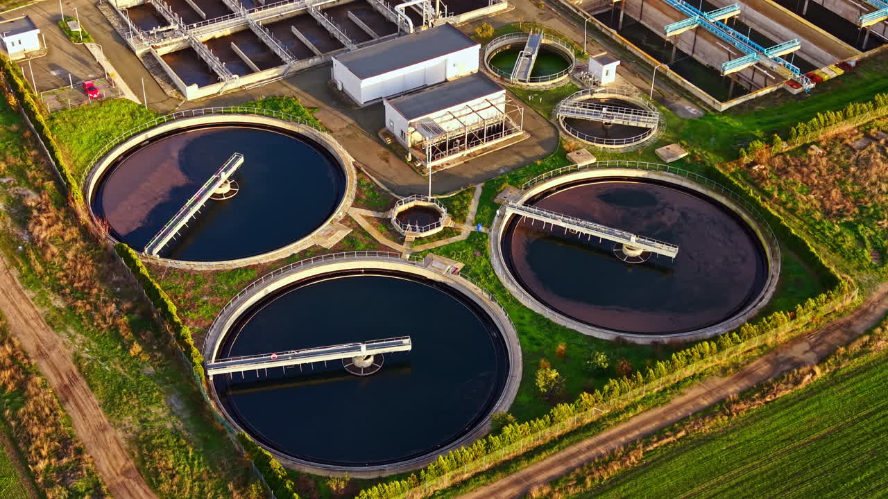 Wastewater treatment facility showcases circular tanks and modern infrastructure amidst lush greenery in a sunny daylight setting