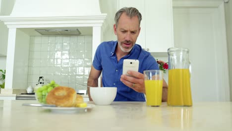 hombre usando teléfono móvil mientras toma el desayuno en la mesa de comedor