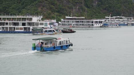 old fishing boats sailing across the sea passing to docked cruise liners in ha long bay, vietnam