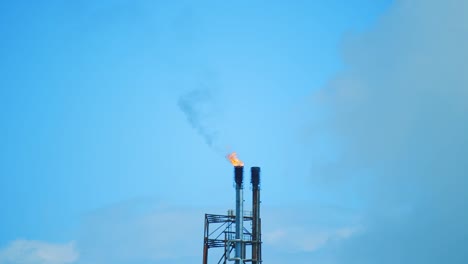 Toma-En-Cámara-Lenta-De-La-Parte-Superior-De-Una-Refinería-Industrial,-Enmarcada-Centralmente,-Que-Muestra-El-Smog-Negro-Contaminante-Que-Se-Emite-En-Un-Cielo-Azul-Claro-En-Curacao