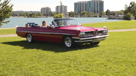 Bride-and-groom-driving-a-retro-red-convertible-into-a-park