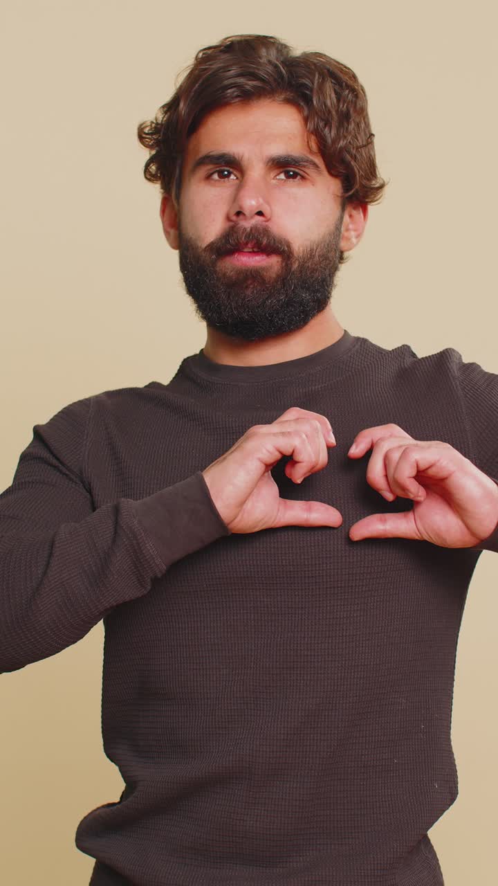Smiling happy lebanese young man makes heart gesture demonstrates love sign on beige background