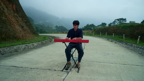 professional pianist sitting playing in middle of a road in the misty outdoors