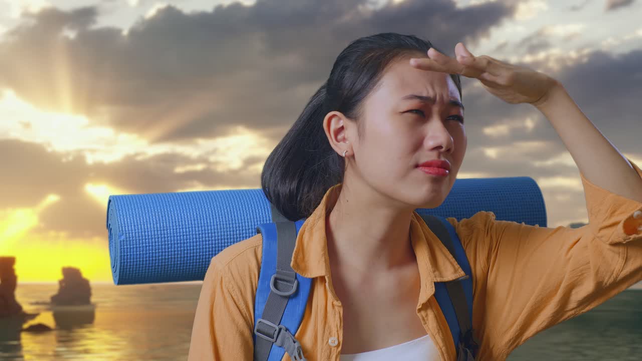 Close Up Of Asian Female Hiker With Mountaineering Backpack Hand Forehead Smiling And Looking Distance While Standing on Beach During Sunset Time