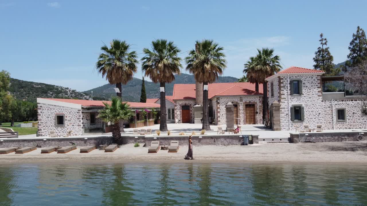 Tourist couple sunbathing in outdoor area of a beachside hotel property, Zaira hotel building and landscape surrounding hills and olive gardens, Lesvos Island, Drone shot