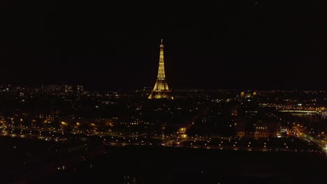 Wide-busy-boulevard-and-illuminated-Eiffel-tower-at-night.-Forwards-fly-above-evening-city.-Beam-of-light-shining-from-top-of-tower.-Paris,-France