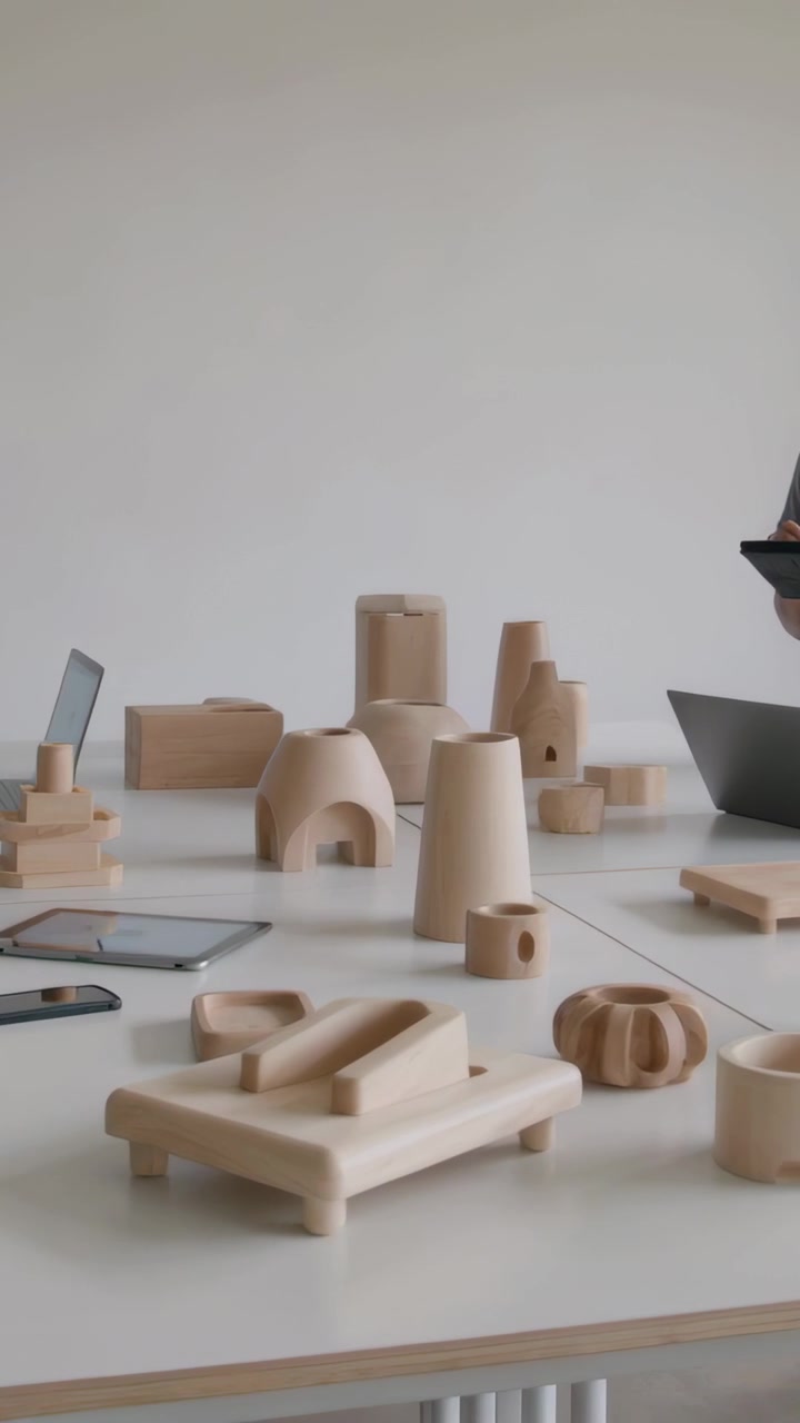 Video verticale: Telecamera che panoramica mostrando un uomo in maglietta grigia che esamina modelli in legno in studio usando un tablet.