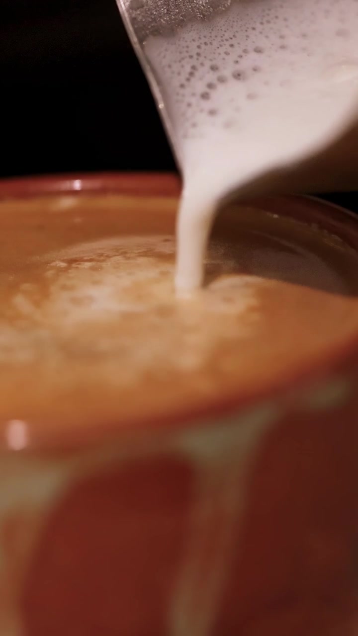Il latte viene versato in una tazza da caffè, creando motivi a spirale. L'illuminazione calda esalta l'atmosfera accogliente.