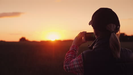 young woman farmer photographing a beautiful sunset over a wheat field 4k video