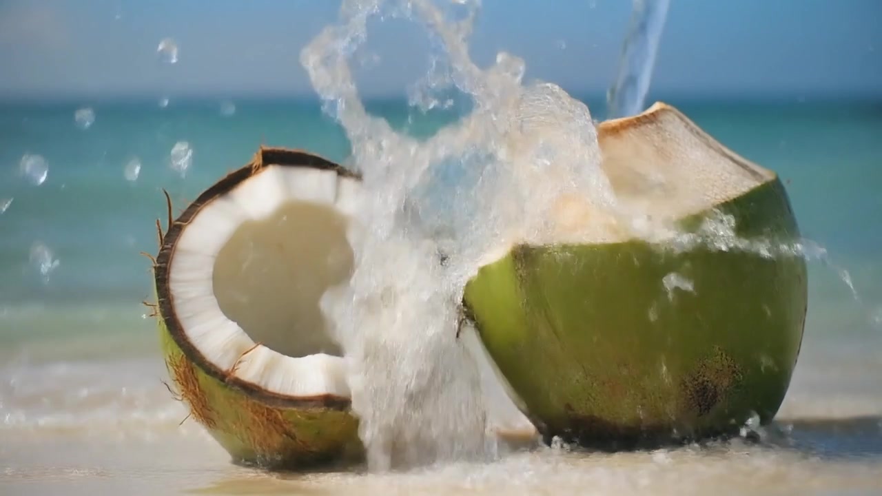 Fresh Coconut Water Pouring onto Halved Coconut on Tropical Beach