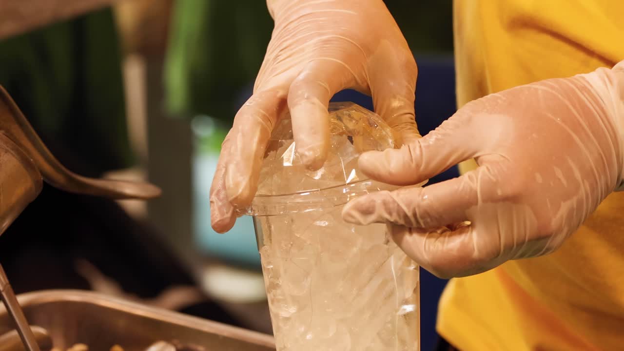 Hands carefully place a lid on a cup filled with ice, showcasing attention to detail and hygiene.