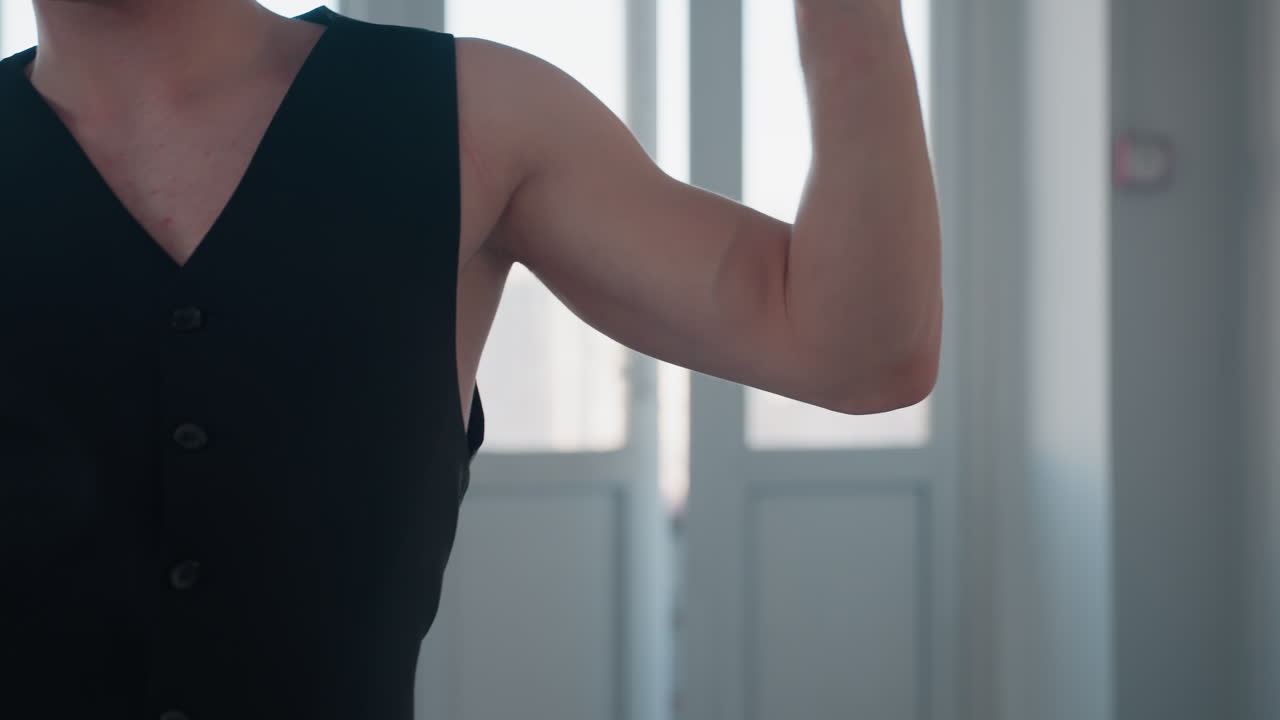 closeup of young man dancing expressively with black belt in hand, arm extended, partial tattoo visible on chest, sunlight streaming through tall windows behind him