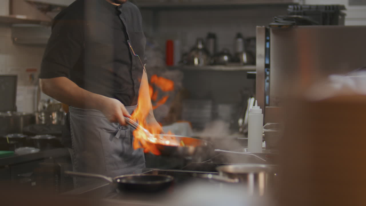 Chef accende la fiamma nella padella e cucina il cibo nella cucina del ristorante.