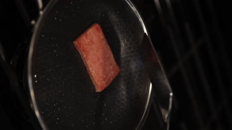 spatula cooking slice of spam meat in stainless steel pan, vertical