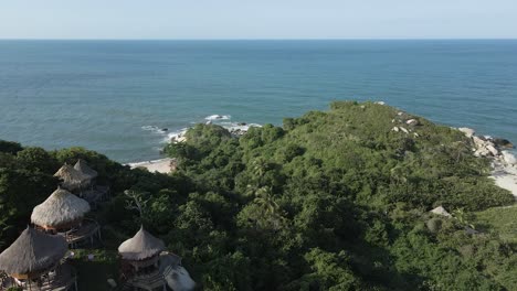 Drone-slowly-pans-above-the-covered-hills-of-Tayrona-rainforest-looking-over-the-vast-Ocean