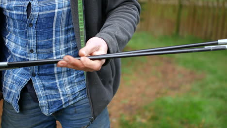 a man putting tent poles together whist pitching a tent camping in a field