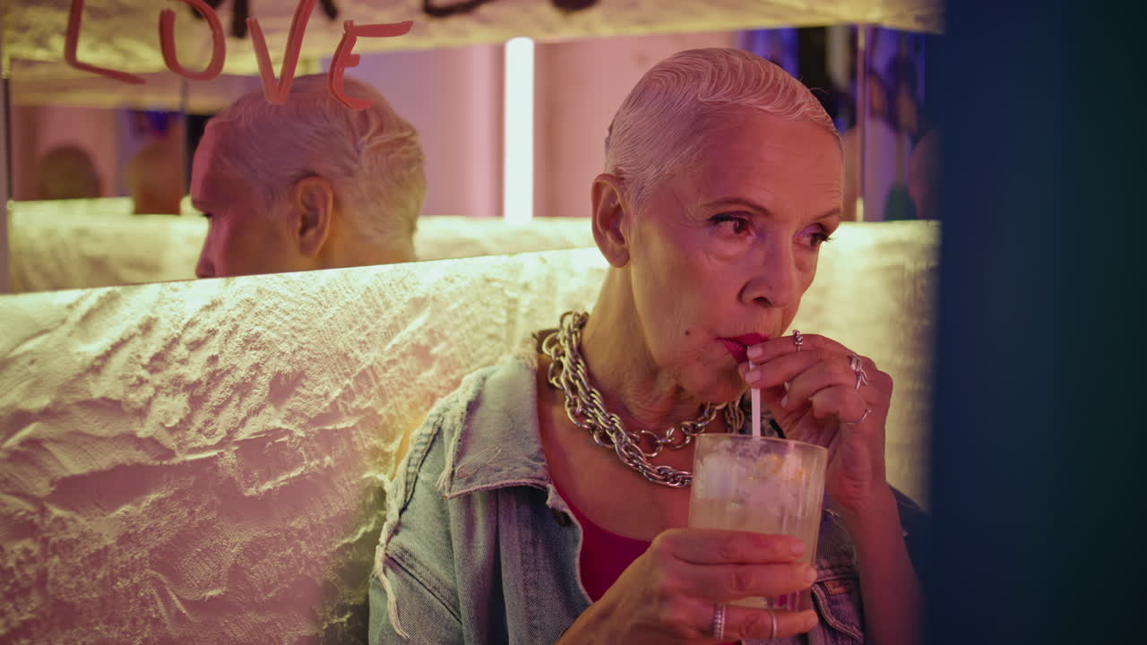 Stylish senior drinking cocktail in evening cafe closeup. Cool mature woman rest