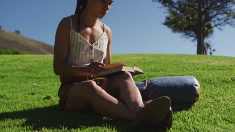 African-american-woman-sitting-on-grass-reading-book-in-park