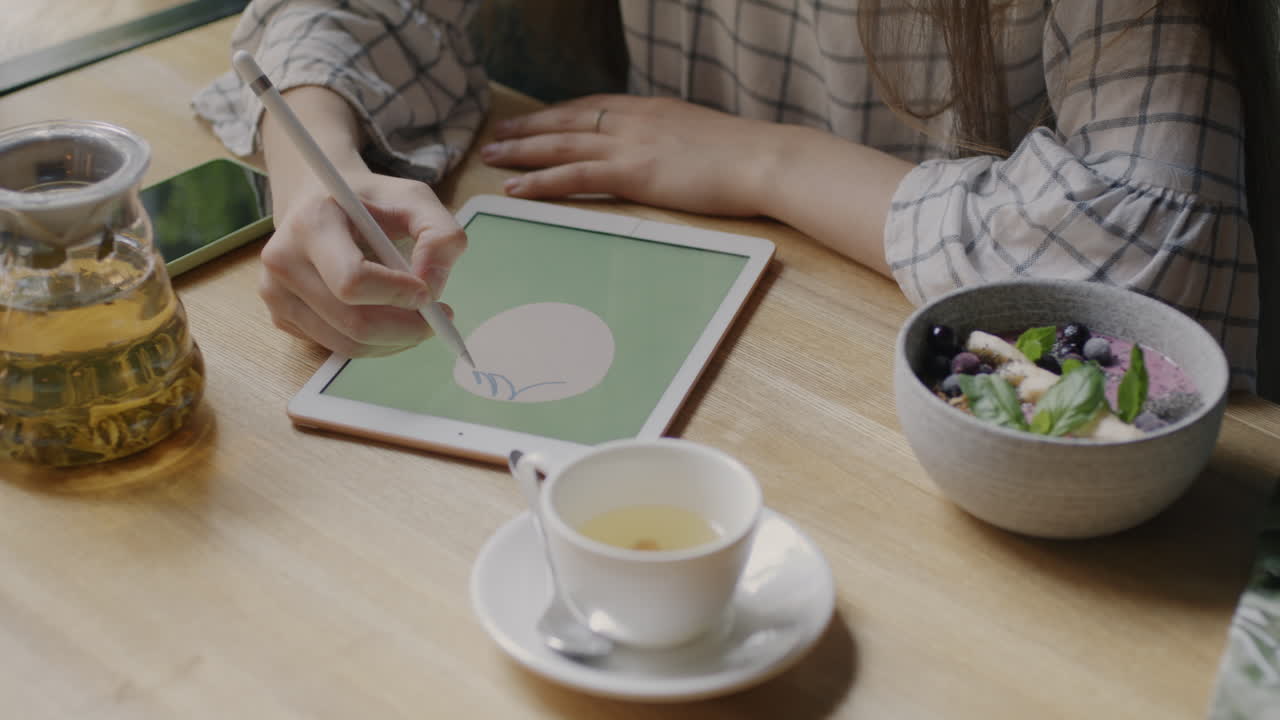 Woman Drawing on Tablet in a Cafe