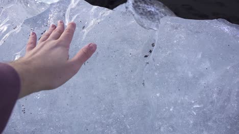 man touching block of ice on seashore