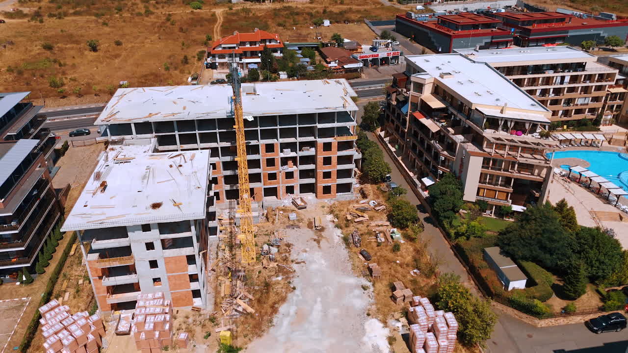 Varna, Bulgaria, 29 June 2025: Construction site next to a bright blue resort pool. The unfinished building and crane stand beside a vibrant hotel with lush green landscaping