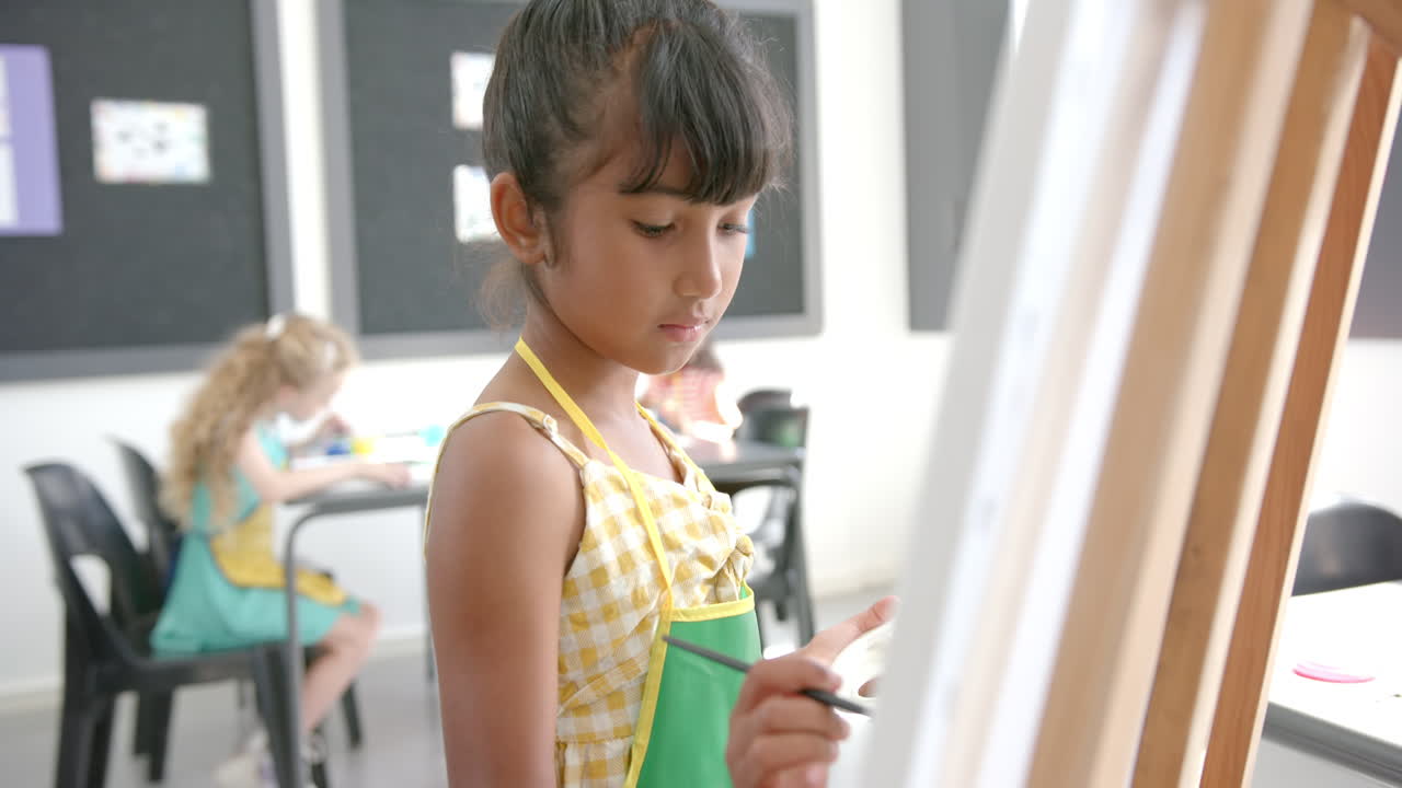 In school, girl painting on canvas in classroom, focusing on artwork